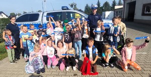 zdjęcie grupowe policjanci z dziećmi które trzymają elementy odblaskowe