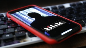 smartfon z postacią i napisem BLIK na ekranie, w tle klawiatura komputerowa