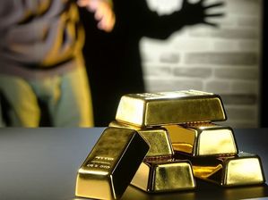 zdjęcie poglądowe: sztabki złota na stole i sylwetka złodzieja