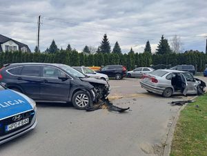 Dwa uszkodzone samochody na jezdni, w tle inne pojazdy. Z lewej strony na pierwszym planie radiowóz