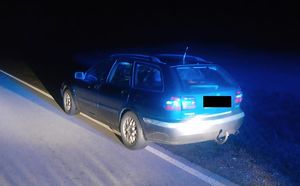 Na zdjęciu widoczny jest stojący na drodze samochód osobowy marki Volvo koloru ciemnego typu kombi. Zdjęcie jest zrobione w porze nocnej