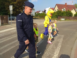 policjant przeprowadza dzieci przez ulicę z maskotką