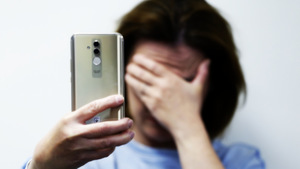 kobieta trzymająca w dłoni telefon i zakrywająca twarz