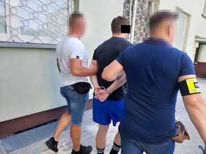 mężczyzna z kajdankami na rękach obok policjanci