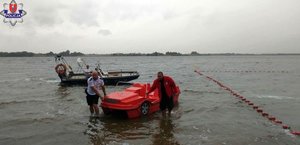 policjant i ratownik WOPR odholowują rower wodny do brzegu. W tle policyjna łódka