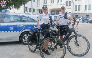 policjant i policjantka przy rowerach, w tle radiowóz