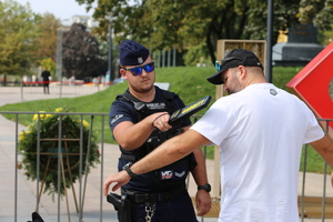 Policjant przy pomocy wykrywacza kontroluje dziennikarza, który che wejść na Plac Litewski