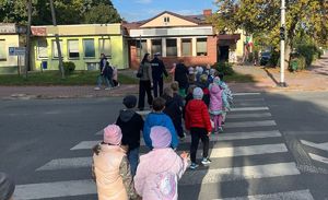 zdjęcie przedstawia grupę kilkunastu uczniów przechodzących przez przejście dla pieszych z sygnalizacją świetlną razem z uczniami przechodzą policjant i nauczyciele