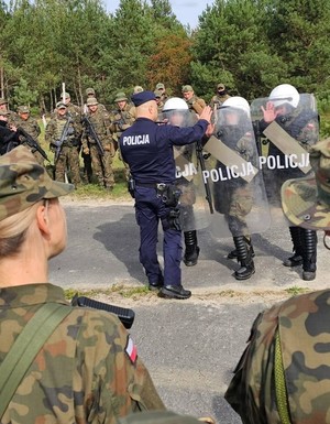 policjant podczas ćwiczeń z żołnierzami prezentuje elementy szkolenia