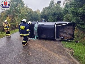 przewrócony na jezdni na lewy bok osobowy Mitsubishi, obok auta stoi trzech strażaków