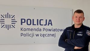 policjant na tle ścianki z napisem Policja Komenda Powiatowa Policji w Łęcznej