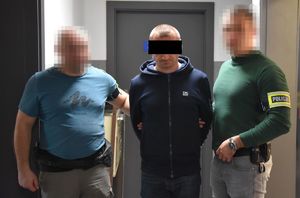 mężczyzna z zasłoniętymi oczami, którego prowadzą policjanci