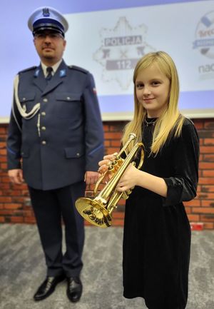 uczestniczka konkursu trzymająca w dłoniach instrument muzyczny, w tle widać policjanta