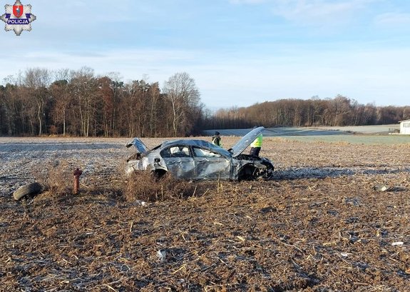 Uszkodzone osobowe BMW w polu, obok niego dwaj policjanci