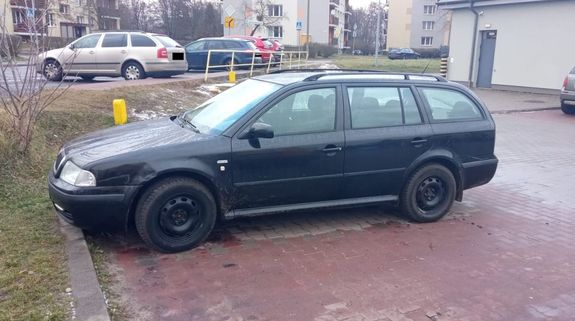 Zdjęcie samochodu osobowego stojącego na parkingu. Samochód marki Skoda koloru czarnego typu kombi. w tle inne pojazdy i budynki zabudowy miejskiej.