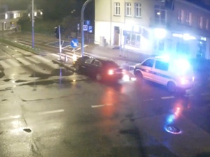 skrzyżowanie dróg, uszkodzony samochód przy słupie sygnalizacji świetlnej, obok radiowóz z włączonymi światłami pojazdu uprzywilejowanego