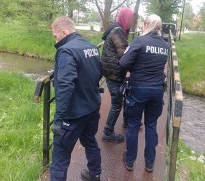 policjantka i policjant z mężczyzną na kładce przy rzece