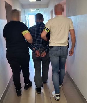 Policjanci prowadzą zatrzymanego mężczyznę.