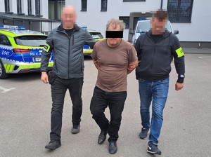 nieumundurowani policjanci prowadzą podejrzanego, w tle ściany budynku i radiowozy