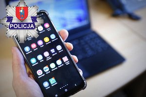 na zdjęciu widoczny telefon trzymany w ręce w tle komputer