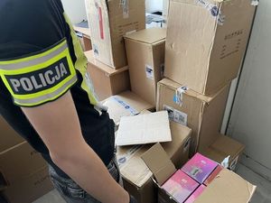 policjant stoi przy kartonach, w których znajdują się zabezpieczone papierosy elektryczne