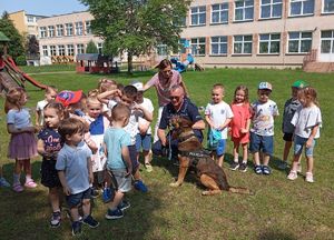 Policjant z psem służbowym, a dookoła niego znajdują się przedszkolaki.