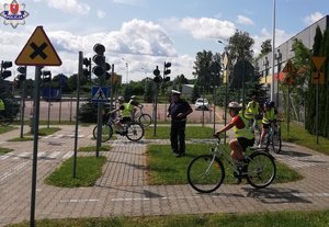 policjant i jeżdżący na rowerach uczniowie na miasteczku rowerowym w czasie egzaminu na kartę rowerową