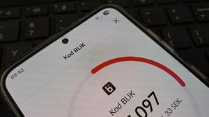 ekran smartfona z kodem blik, w tle klawiatura laptopa