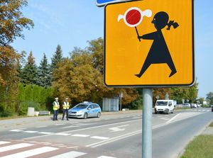 Policjanci podczas nadzoru nad przejściem dla pieszych na pierwszym palnie znak Agatka informacyjny