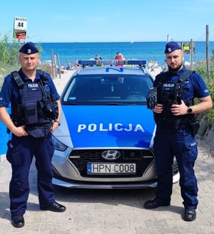 dwóch umundurowanych policjantów stoi przy oznakowanym radiowozie, w tle widać morze Bałtyckie