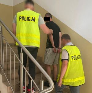 policjanci prowadzący po schodach zatrzymanego w kajdankach