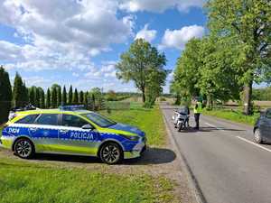 Policjanci podczas kontroli drogowej obok stoi radiowóz policji oznakowany
