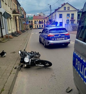motocykl leży na jezdni, obok stoją oznakowane radiowozy policyjne z włączonymi sygnałami świetlnymi