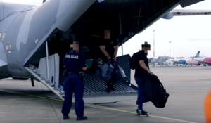 policjant zabezpiecza konwój zatrzymanych osób, które wysiadają z samolotu