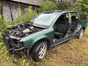 stojący w zaroślach pojazd z widocznymi uszkodzeniami, częściowo rozebrany z drzwi i maski