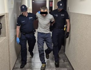 Policjanci prowadzą zatrzymanego 37-latka po korytarzu komendy
