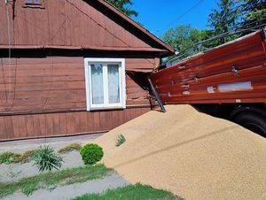wysypane zboże na ziemi, przyczepa wbita w drewniany dom