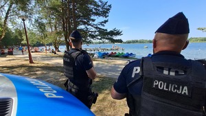 policjanci przed oznakowanym radiowozem patrzący w kierunku plaży i jeziora
