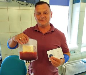 policjant stojący w gabinecie medycznym z trzymanym w ręku woreczkiem z oddanym szpikiem kostnym i legitymacją dawcy