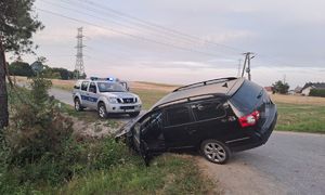 Uszkodzony samochód w rowie i stojący na jezdni policyjny radiowóz.
