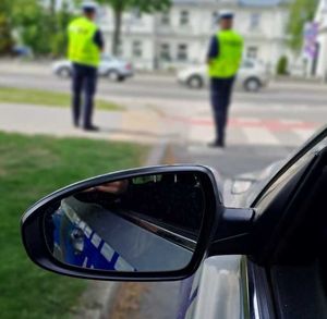 lusterko boczne radiowozu, na drugim planie dwóch umundurowanych policjantów z wydziału ruchu drogowego