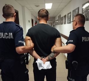 dwaj umundurowani policjanci prowadzą korytarzem zatrzymanego mężczyznę