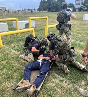 ranny człowiek na noszach, obok policyjni komandosi na otwartej przestrzeni