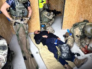 policjant tamuje krwotok u poszkodowanego leżącego na podłodze, kolejni policjanci pilnują bezpieczeństwa