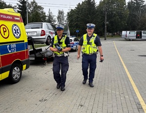 dwaj policjanci z drogówki przechodzą obok karetki pogotowia