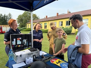 policjantki rozmawiają z Prezydentem Miasta oraz Zastępcą Komendanta PSP oraz dzieckiem które przyszlo obejrzeć stoisko