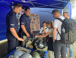 policjanci na stoisku podczas pikniku prezentujący sprzęt mężczyznom z dziećmi