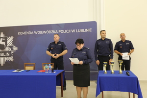 kadrowa odczytuje zwycięzców. Z tyłu komendant i policjanci