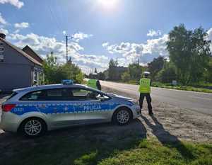 Policjant podczas nadzoru nad ruchem na drodze obok radiowóz