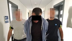 policjanci prowadzą zatrzymanego oszusta